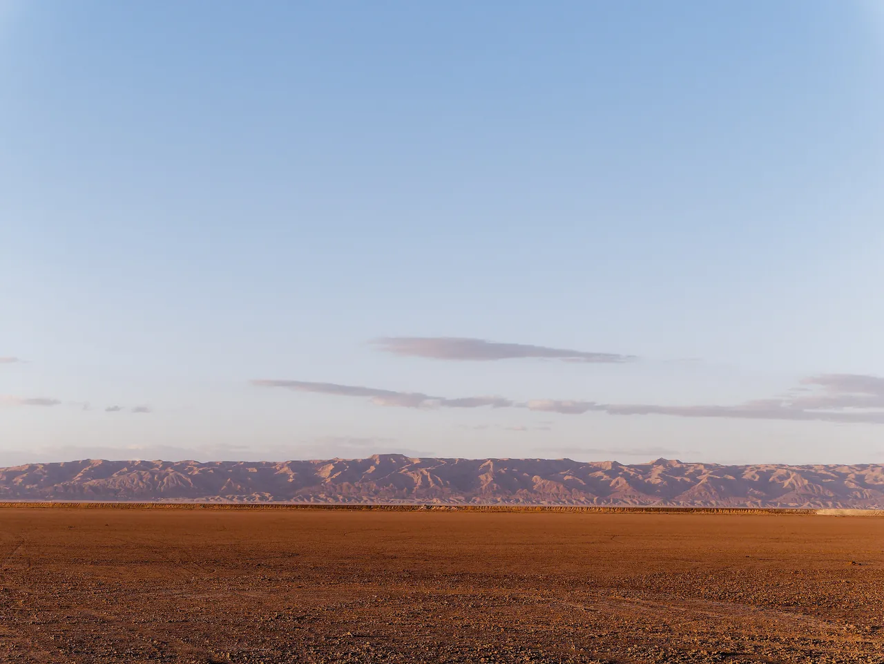 Le Chott el Djerid à l'heure dorée, sol ocre et grand ciel pâle, montagnes au loin